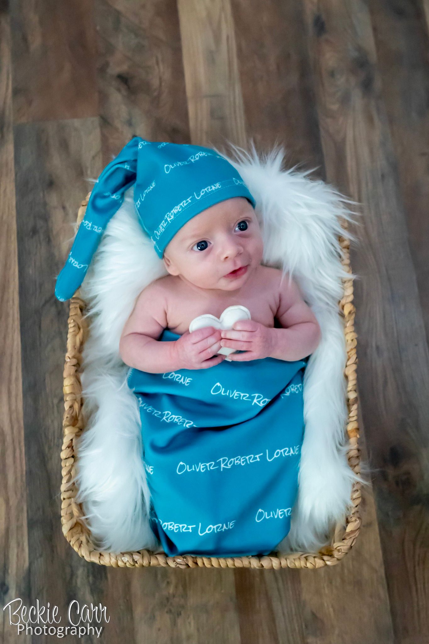 Newborn baby named Oliver Robert Loran swaddled in a blue personalized blanket in a basket.