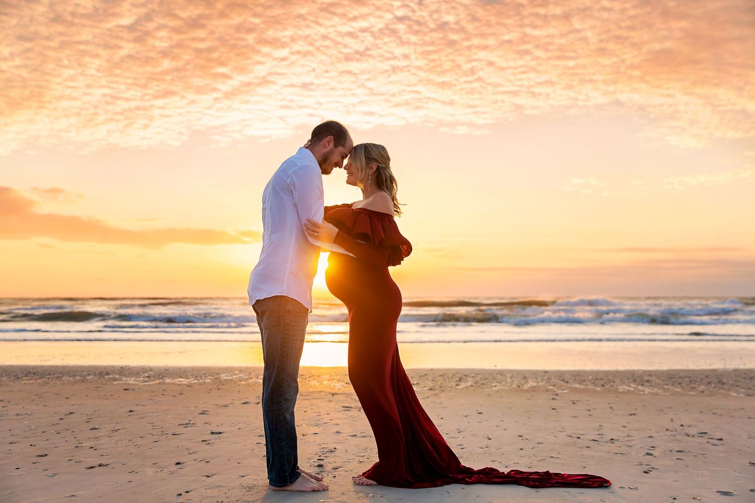 A couple embraces on the beach during a dramatic orange sunset.