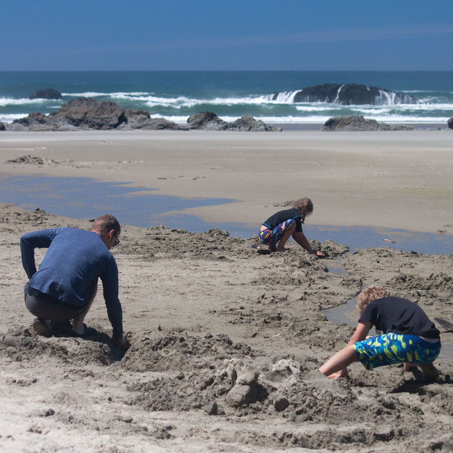 father, son, and daughter all digging in the sand on the Oregon coast