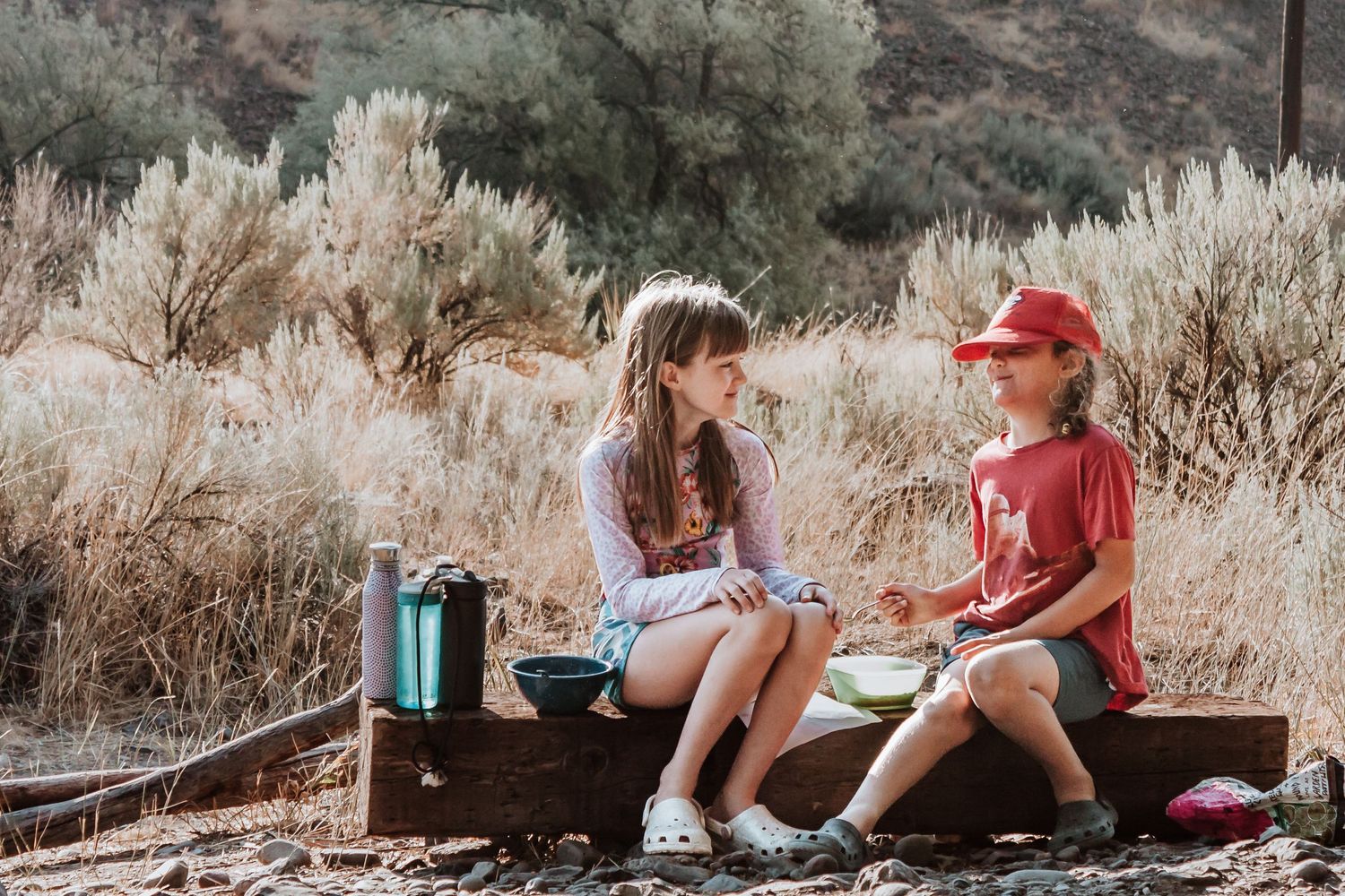 two preteens laughing on a log at a campsite