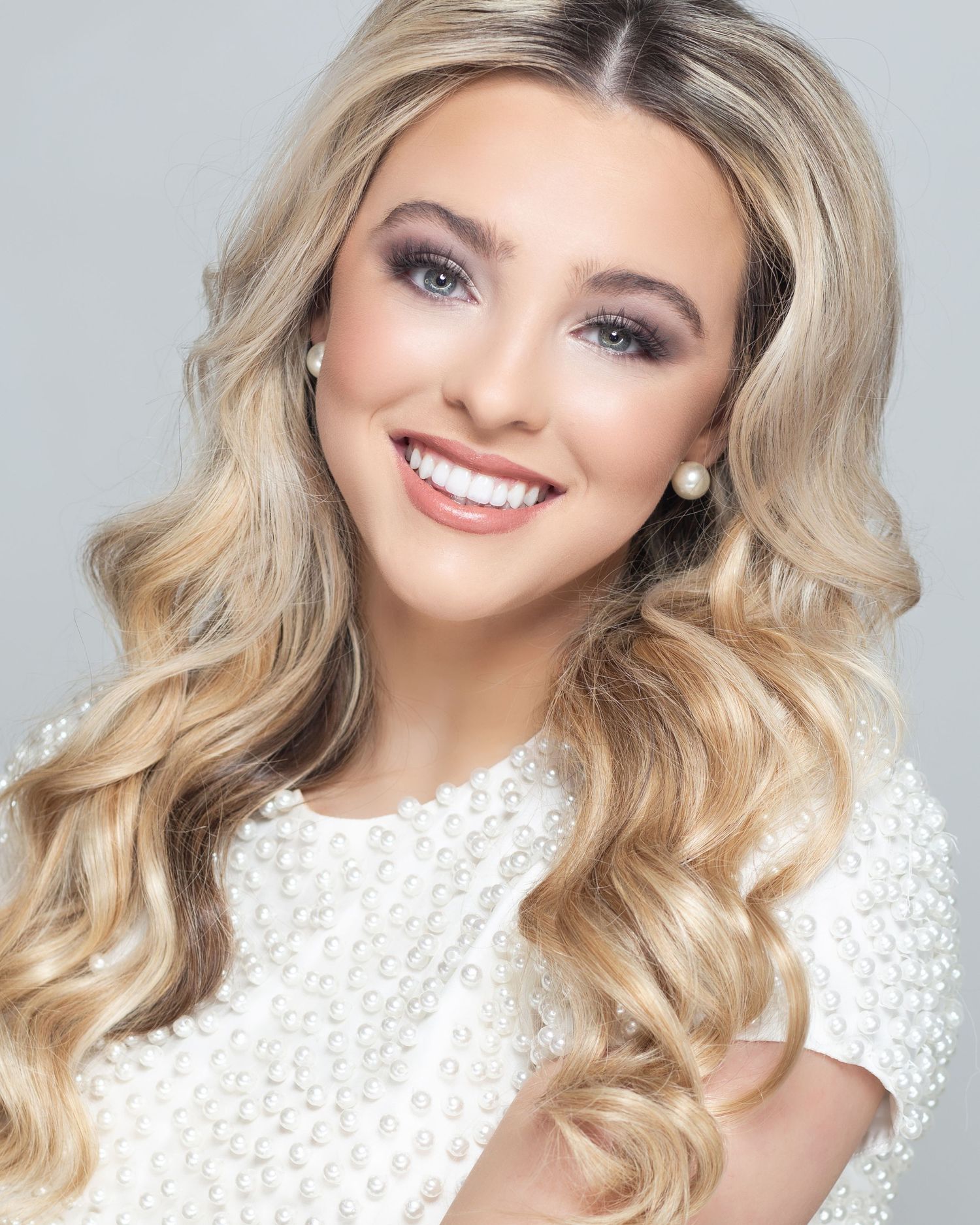 Beauty portrait in white textured top with flowing blonde waves and pearl earrings.