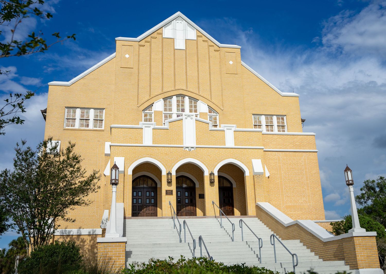 Yellow brick church exterior featuring white architectural details and concrete steps.