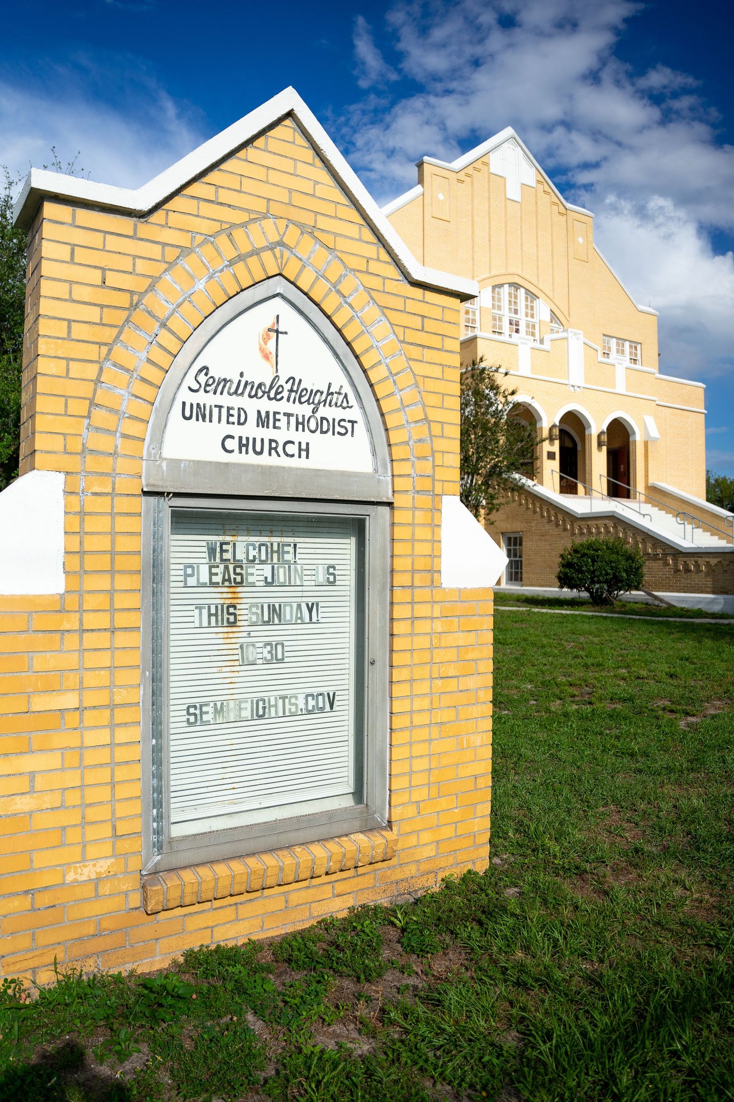 Church signage board constructed with yellow bricks and white trim against a bright blue sky.