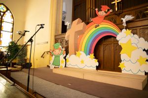 Rainbow and cloud cutout decorations displayed on a wooden church altar platform.