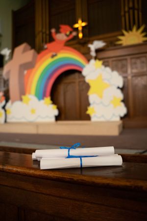 Rainbow and cloud decorations with rolled diplomas on wooden church altar.