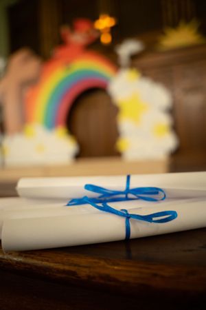 White diplomas tied with blue ribbons displayed in front of rainbow backdrop decorations.