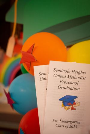 Preschool graduation programs displayed among colorful celebration balloons.