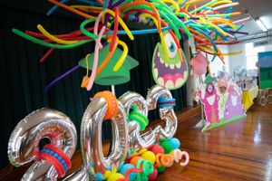 Monster-themed celebration decor with silver balloon numbers and colorful streamers suspended from above.