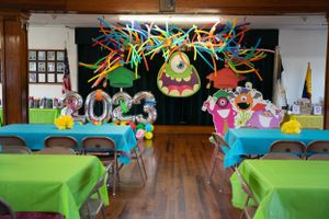 Wide view of a decorated indoor space with green tables and monster party decorations hanging overhead.