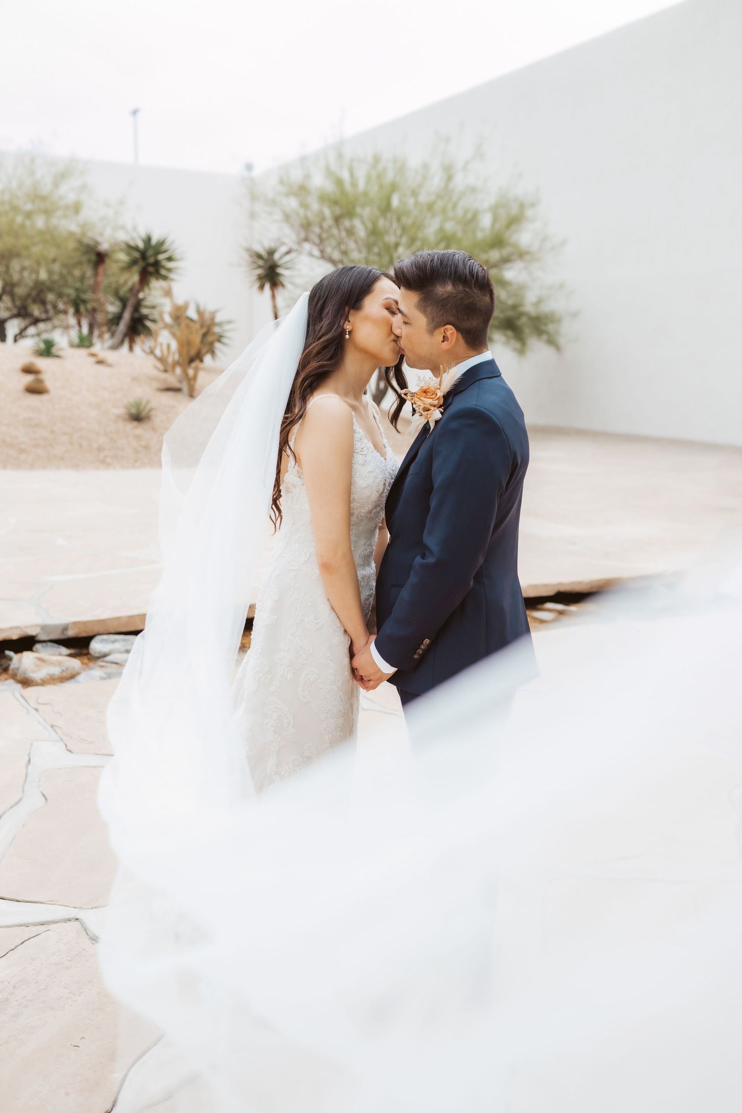 Romantic desert wedding portrait with flowing veil in soft light.