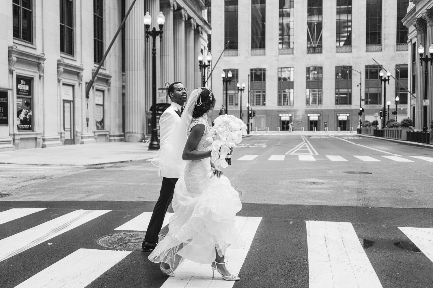 A wedding couple dances joyfully in the middle of a city crosswalk in black and white.