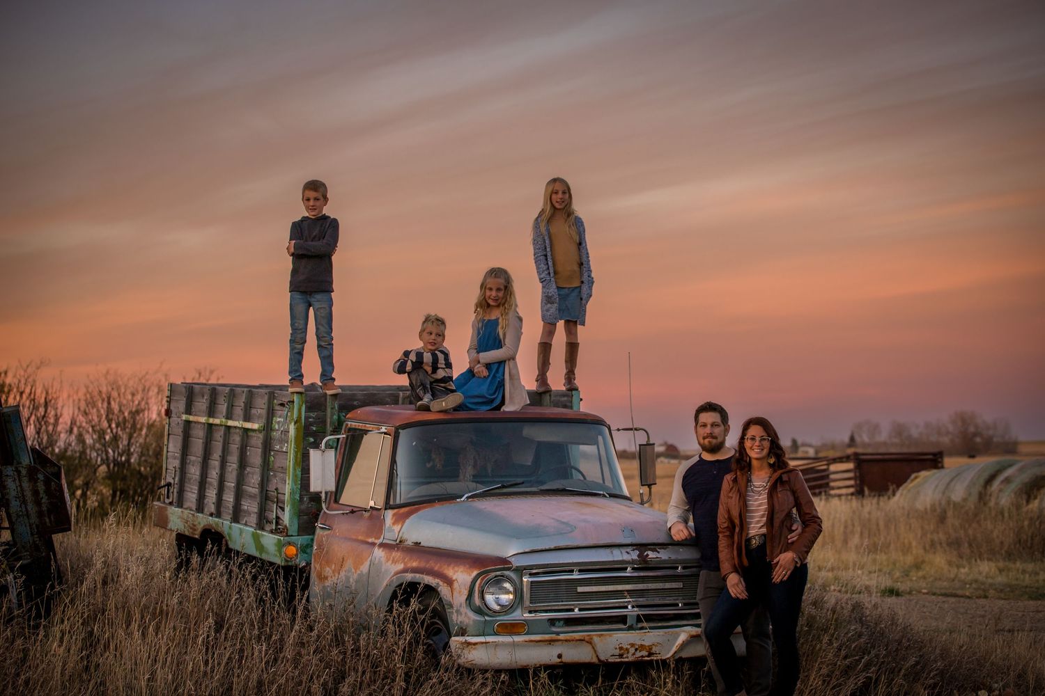Group of friends gathered on vintage truck during golden sunset in rural field.