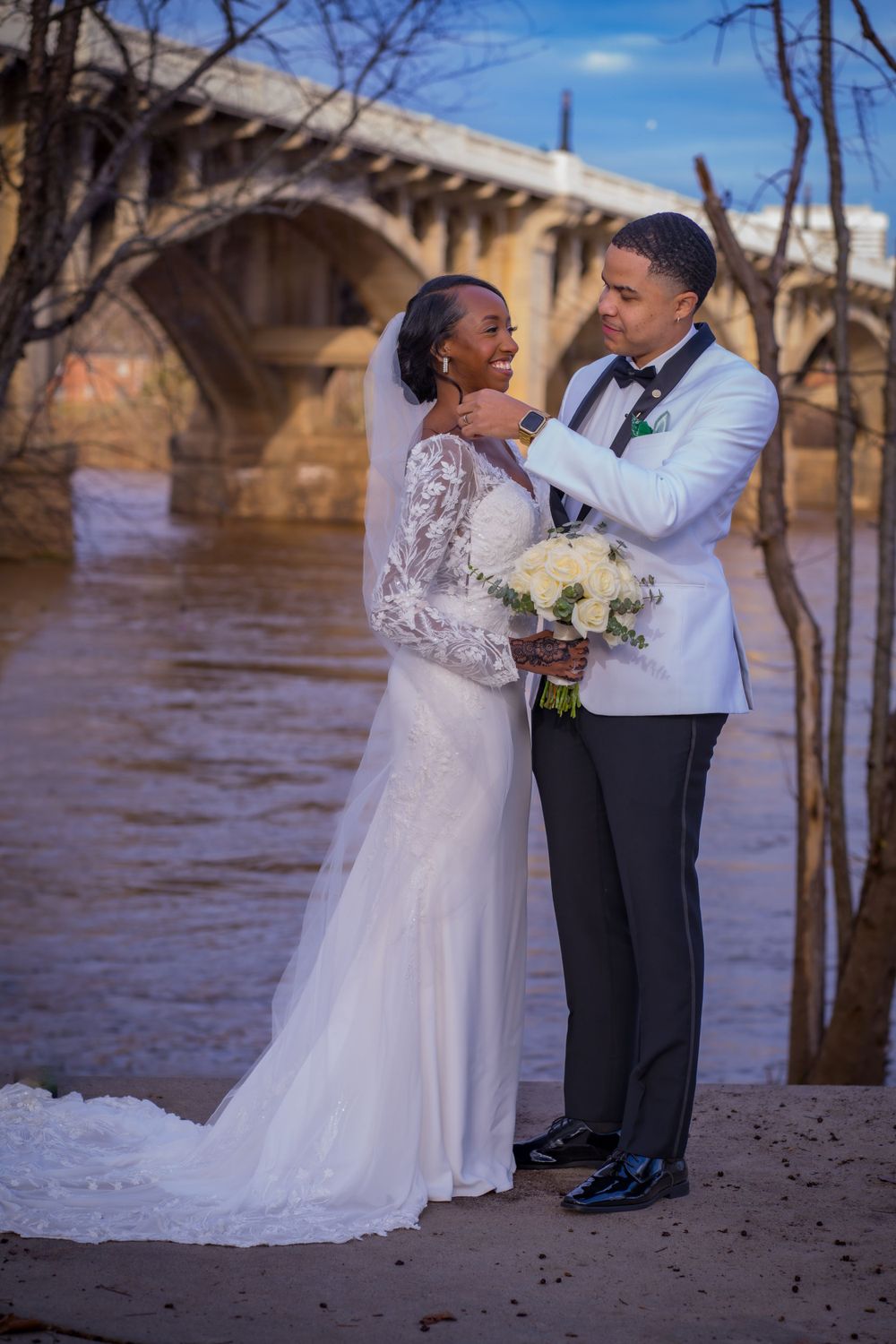 A romantic wedding portrait of a couple by a bridge with the bride holding a white bouquet.