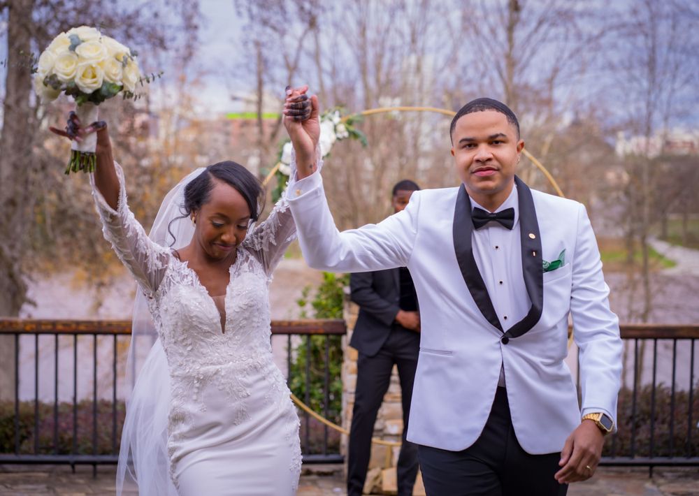 A newlywed couple celebrates with raised arms and bouquet on their wedding day.