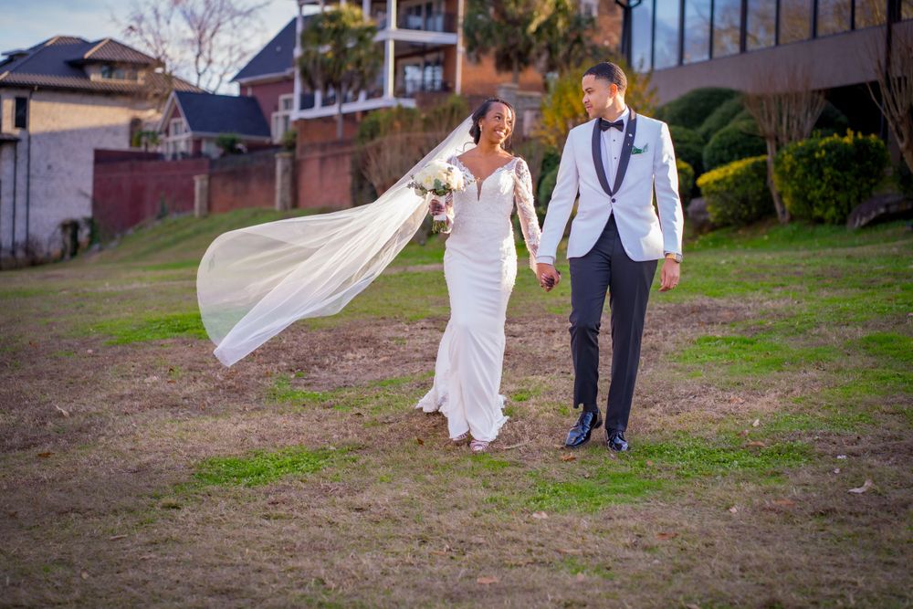 A wedding couple walks together on grass with the bride's veil flowing in the wind.