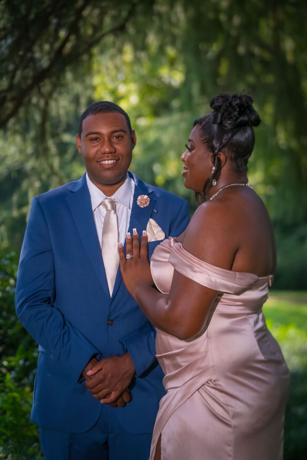 A couple in formal attire shares a candid moment in a garden setting.