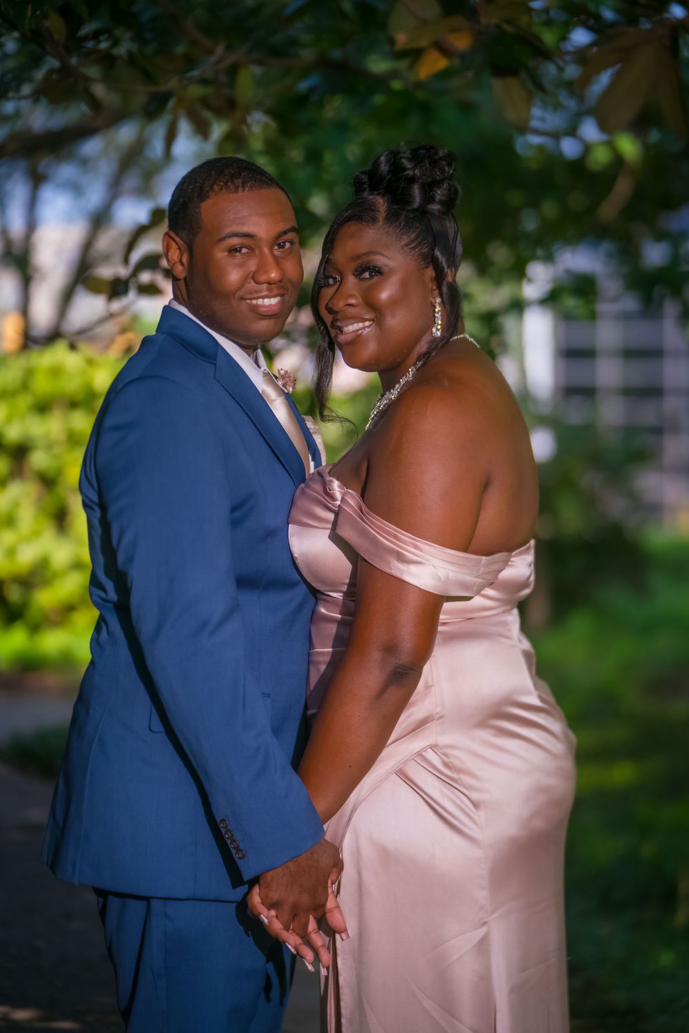 A couple pose intimately together in formal attire against a green outdoor background.