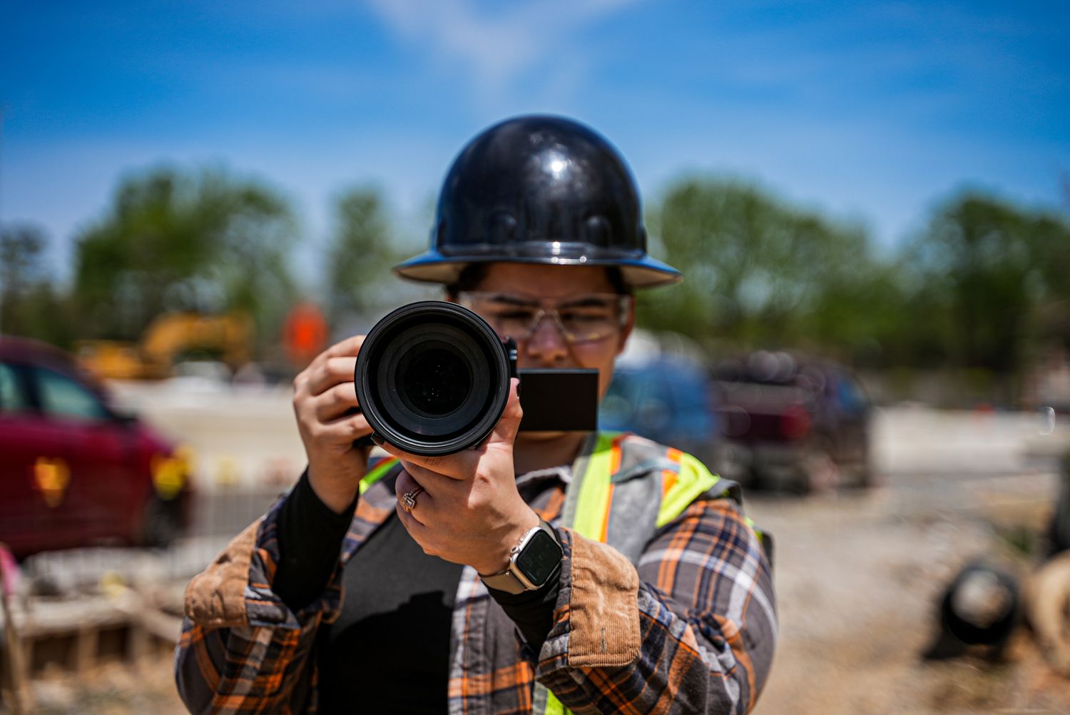 Construction site photographer wearing hard hat and safety vest with camera.