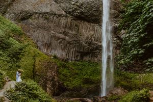 Tall cascading waterfall flows through lush green forest in Oregon's Columbia River Gorge.
