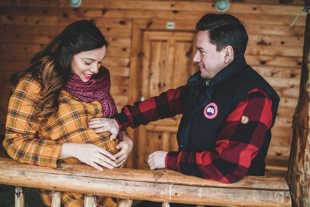 An intimate maternity moment captured on wooden cabin porch during winter photoshoot.