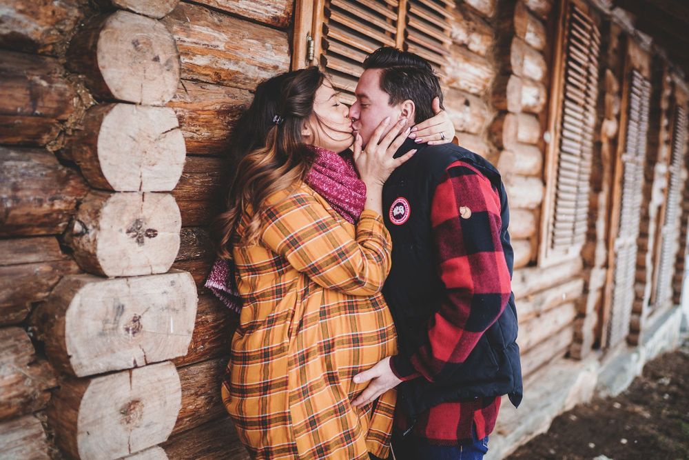 Romantic winter scene of couple embracing against log cabin wall.