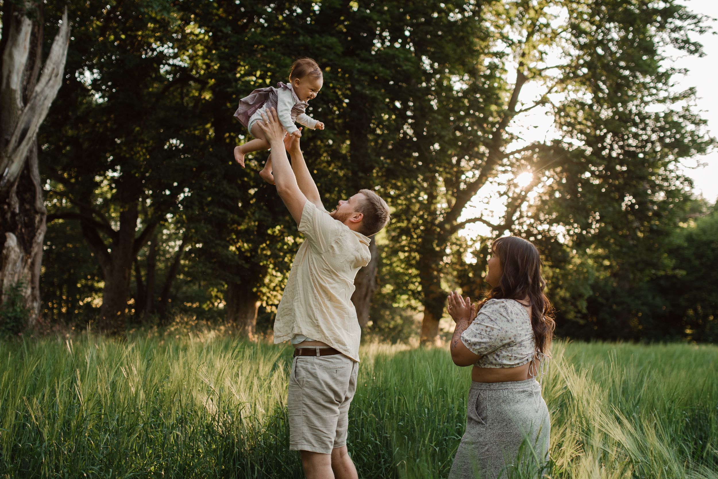 Family plays together in tall grass during golden hour sunset.