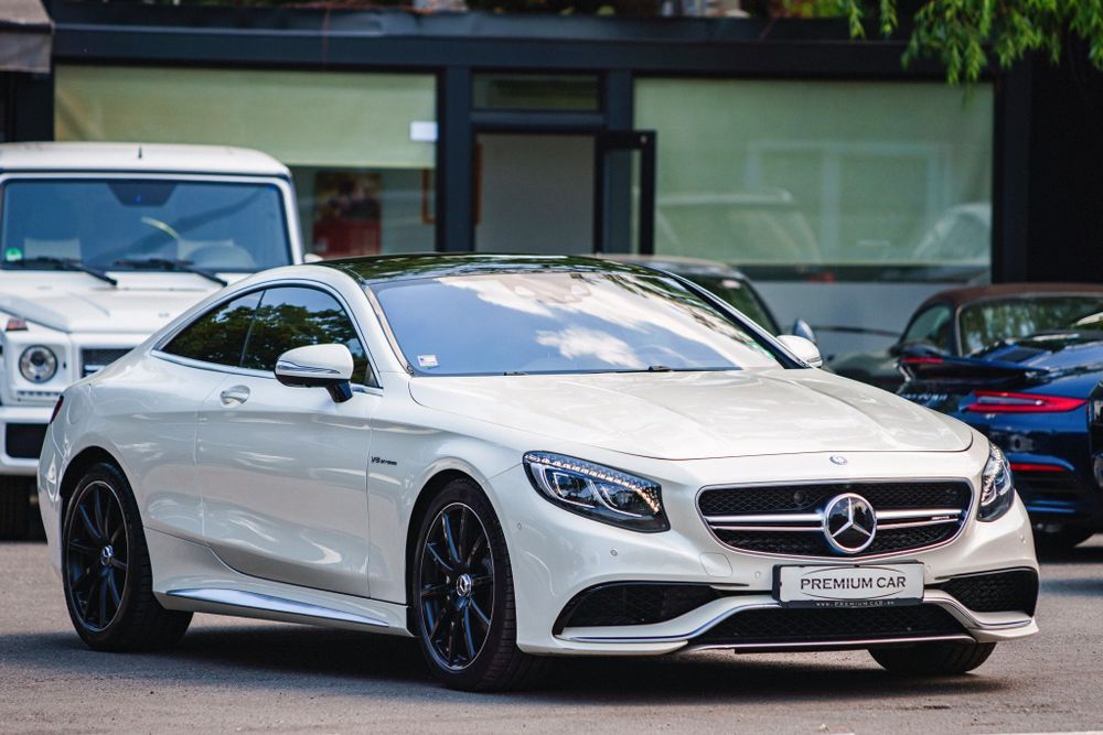White Mercedes-Benz S63 AMG coupe with black wheels parked outside.