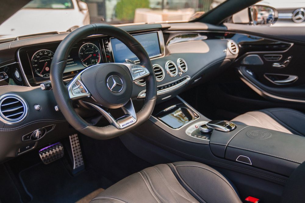 Interior view of a modern Mercedes-Benz luxury car showing black leather dashboard, steering wheel and digital displays.