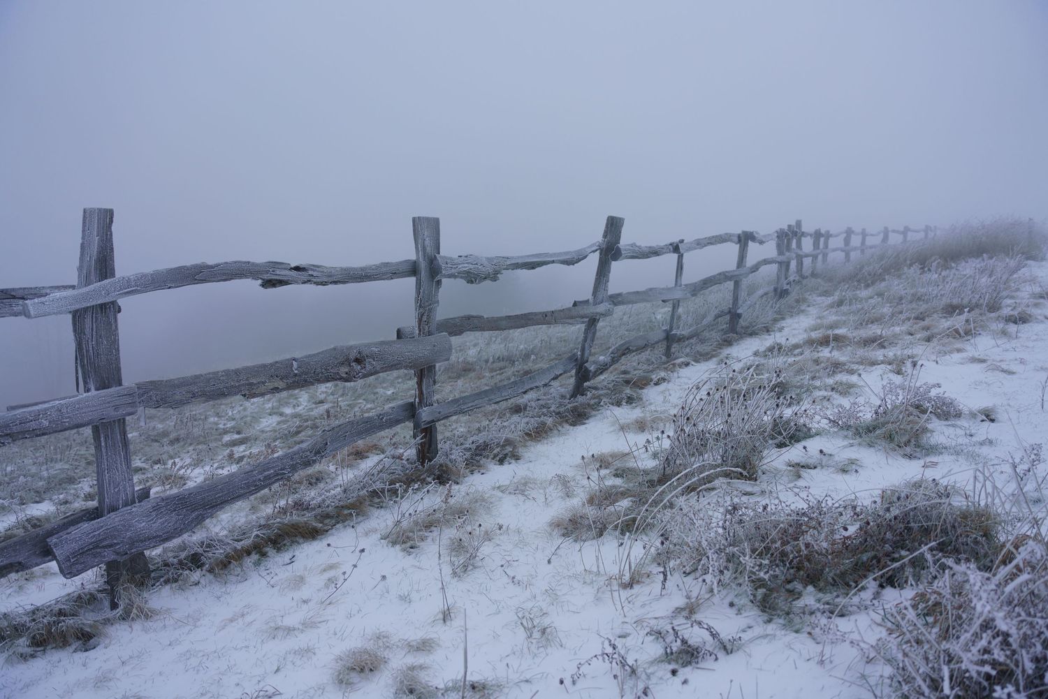 A snow-dusted fence on a cloudy day atop Max Patch.