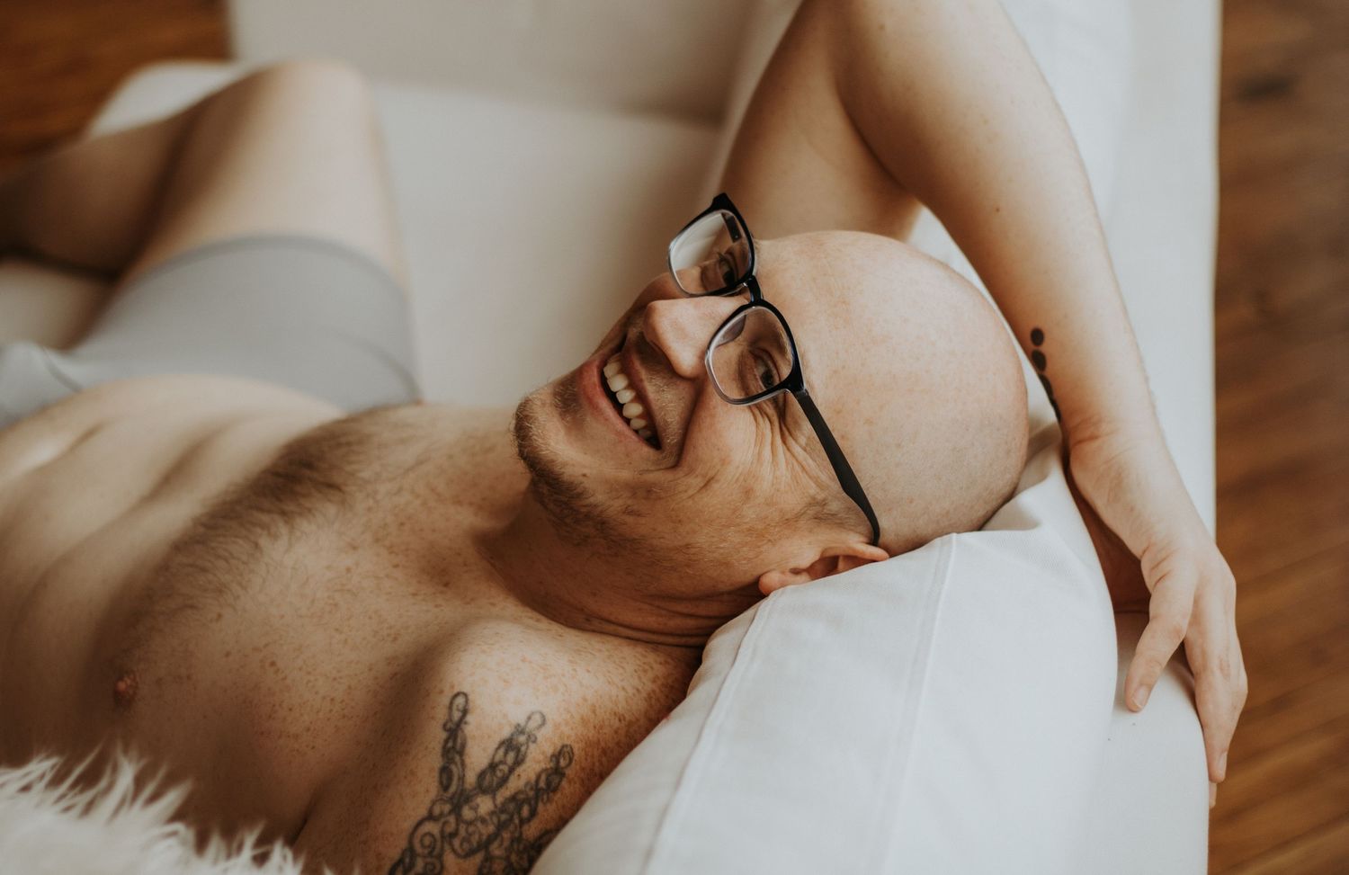 Man wearing glasses lies back on cream couch with joyful expression while relaxing.