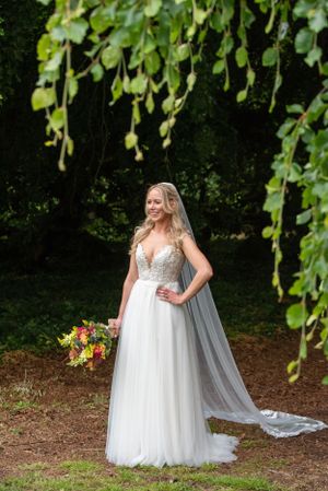 Bride in flowing white gown poses under hanging foliage with colorful bouquet at the stunning Bellinter House