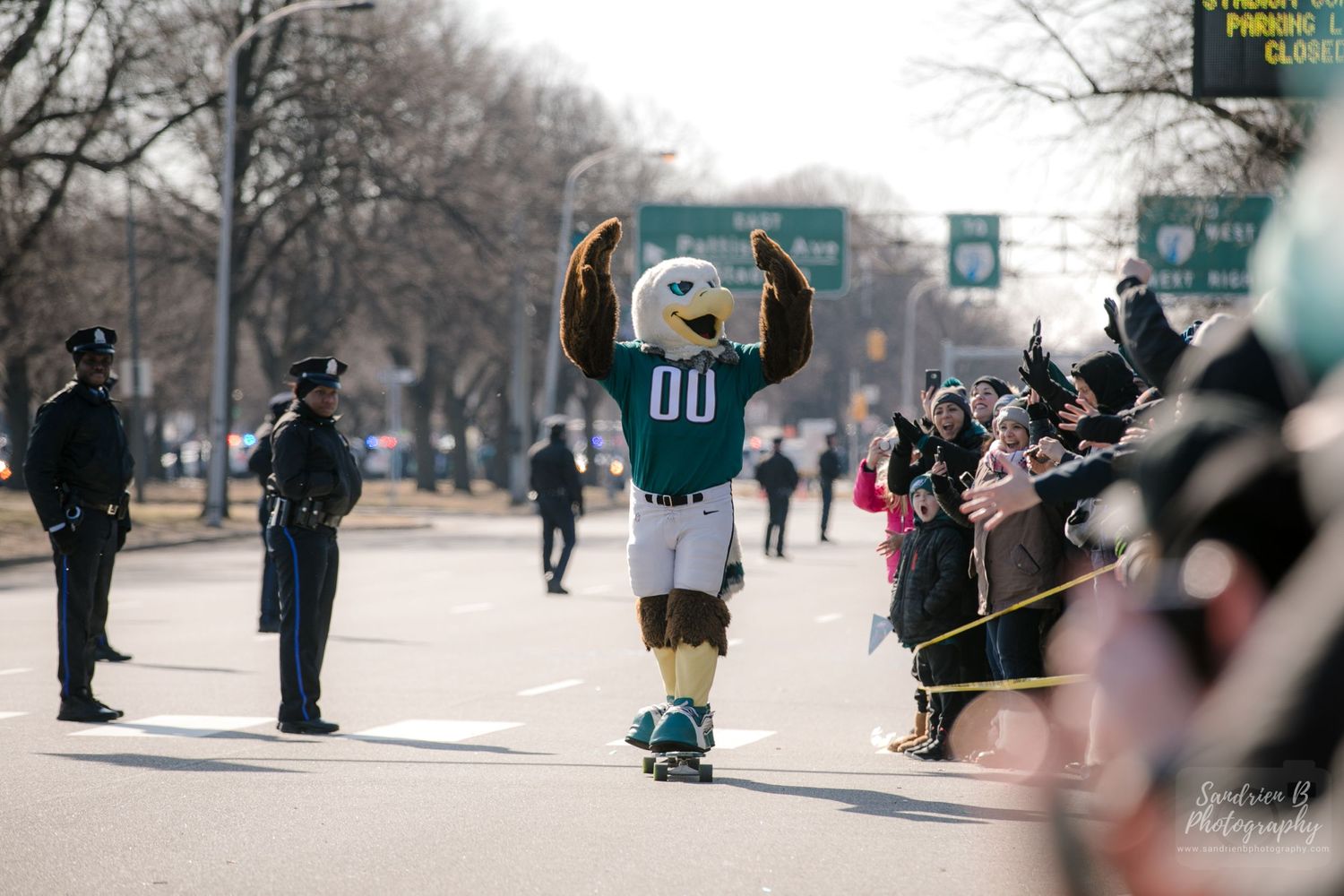 Sports mascot high-fives spectators along parade route while police officers watch.