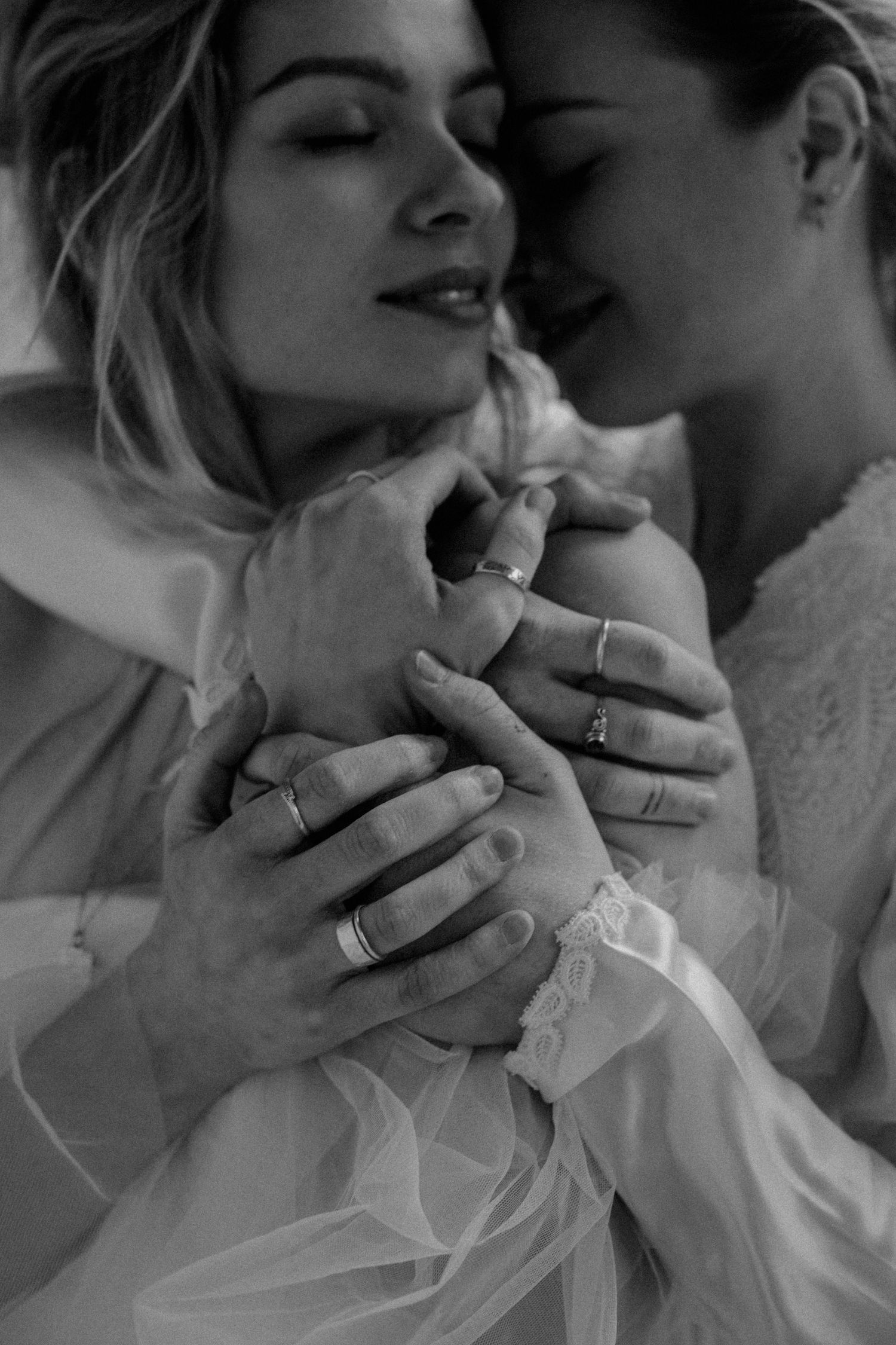 Intimate black and white photograph of tender embrace with interlocked hands.