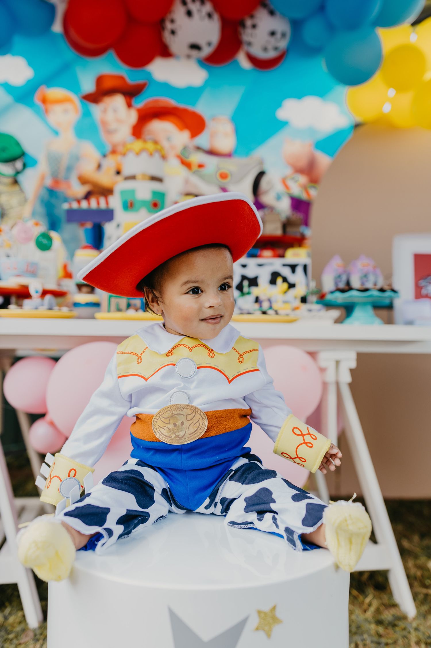 Baby dressed as Toy Story's Jessie sits in decorated chair at themed birthday party.