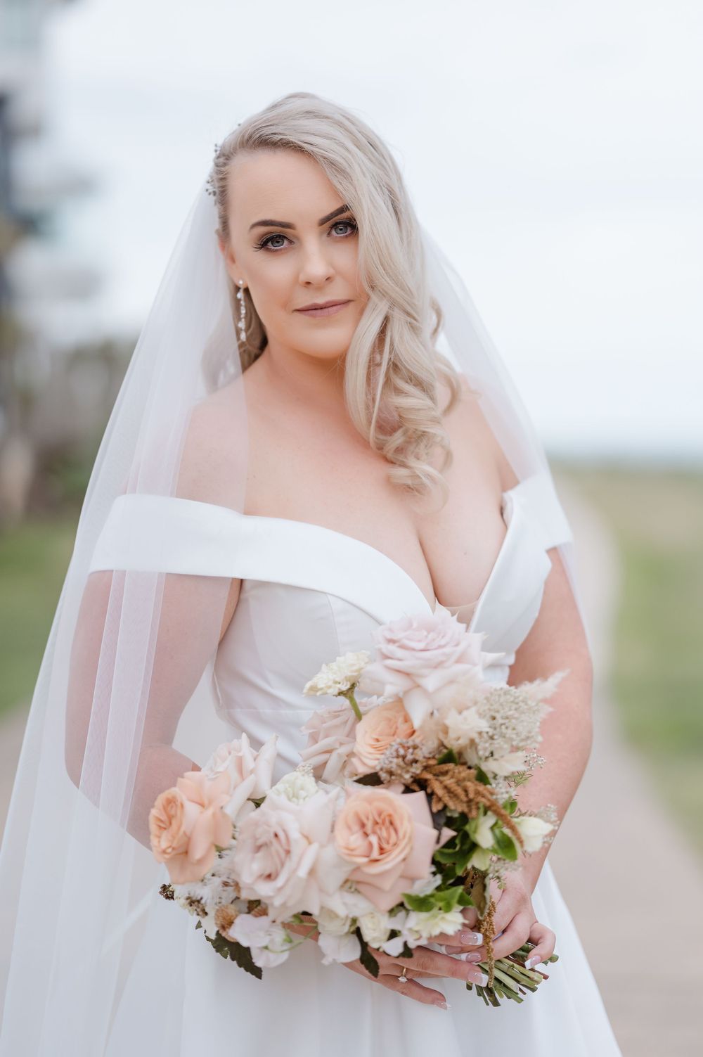 Romantic bridal portrait showcasing an off-shoulder white gown and peach rose bouquet.