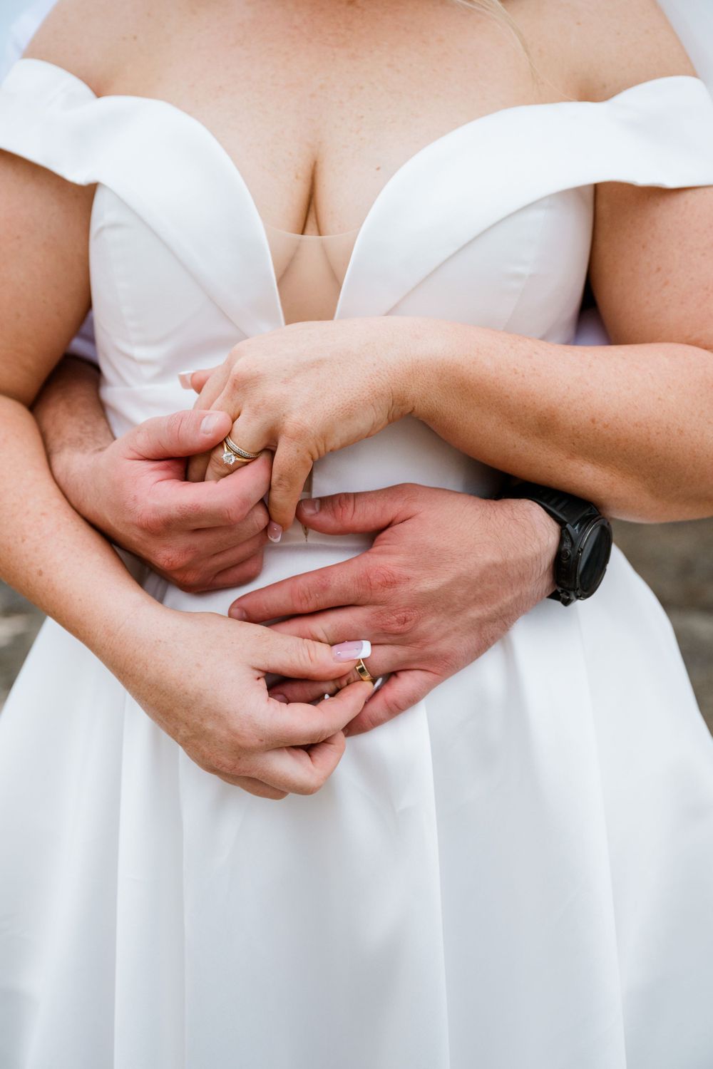 Close-up detail of hands adjusting wedding ring on finger against white dress.