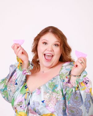 A person in a floral dress holds up pink items with an excited expression.
