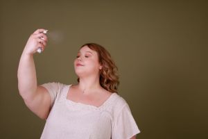 A person in white sprays beauty product with eyes closed in a serene pose.