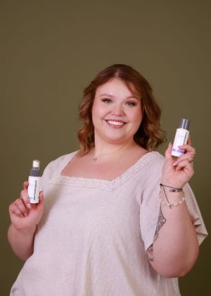 A person in white holding up beauty product bottles with a cheerful expression.
