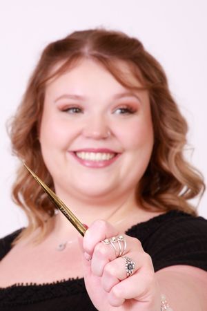 Person displaying gold makeup brush while smiling against light background.