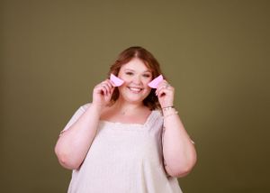 A person in white making playful expressions while holding pink beauty tools.