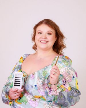 Woman in colorful floral print top poses with beauty products against white background.