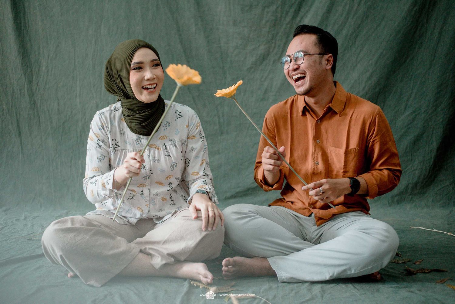 A playful couple sharing tangerines while sitting cross-legged on the floor during a photo session.