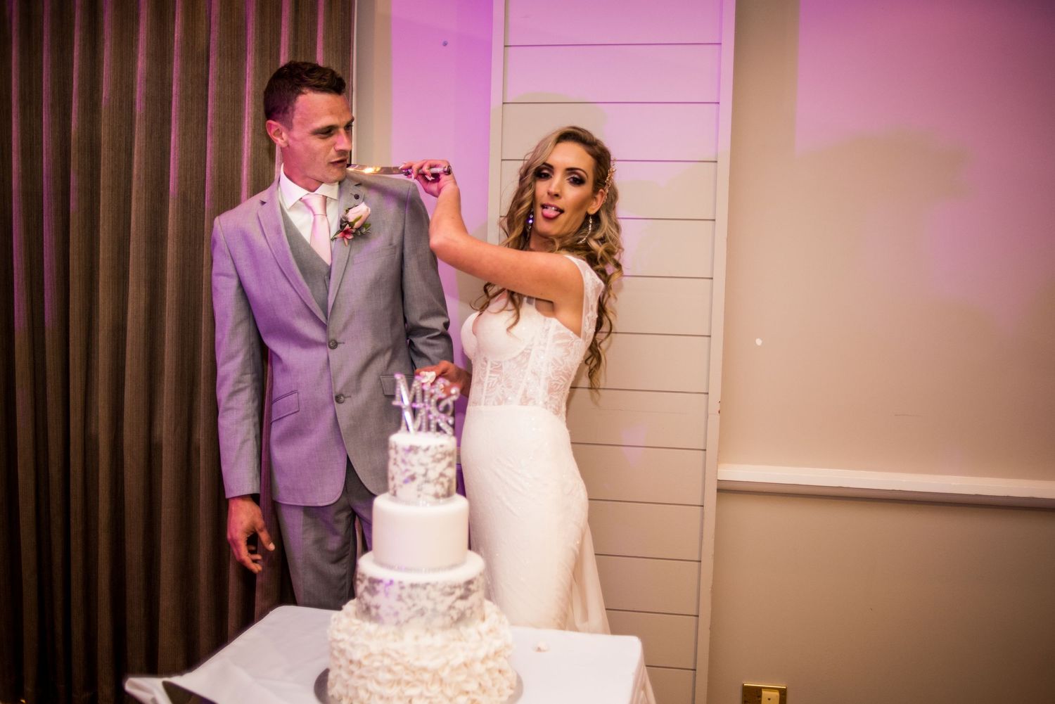 Cake Cutting, Bride and Groom, Grey suit, Knife to the grooms throat, bride with tongue sticking out. Edmonton wedding