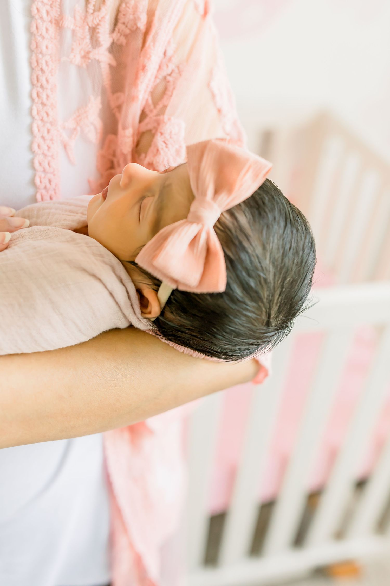 Infant wearing pink bow headband being held during professional photography session.