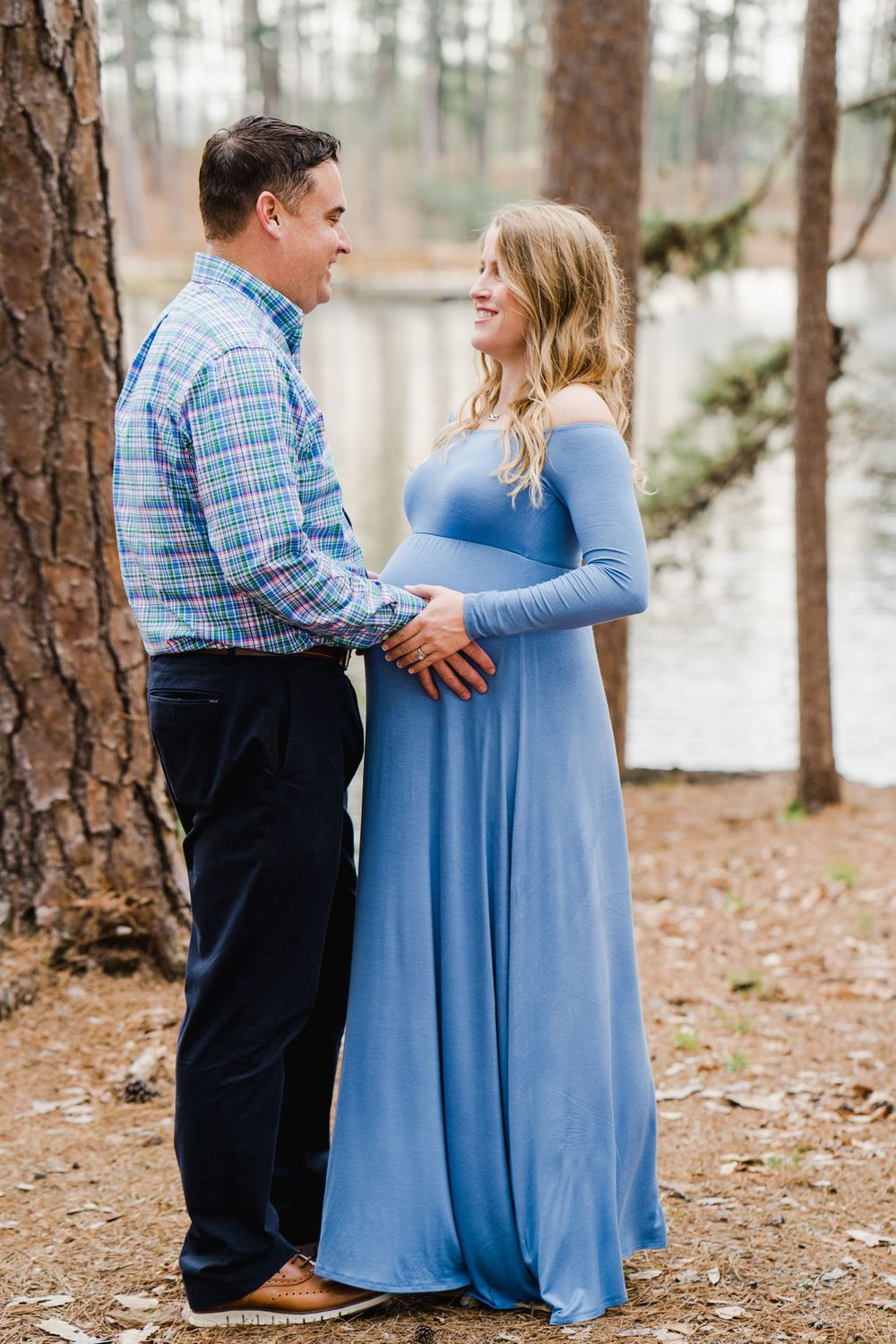 Couple shares tender moment during outdoor maternity photo session by lake.