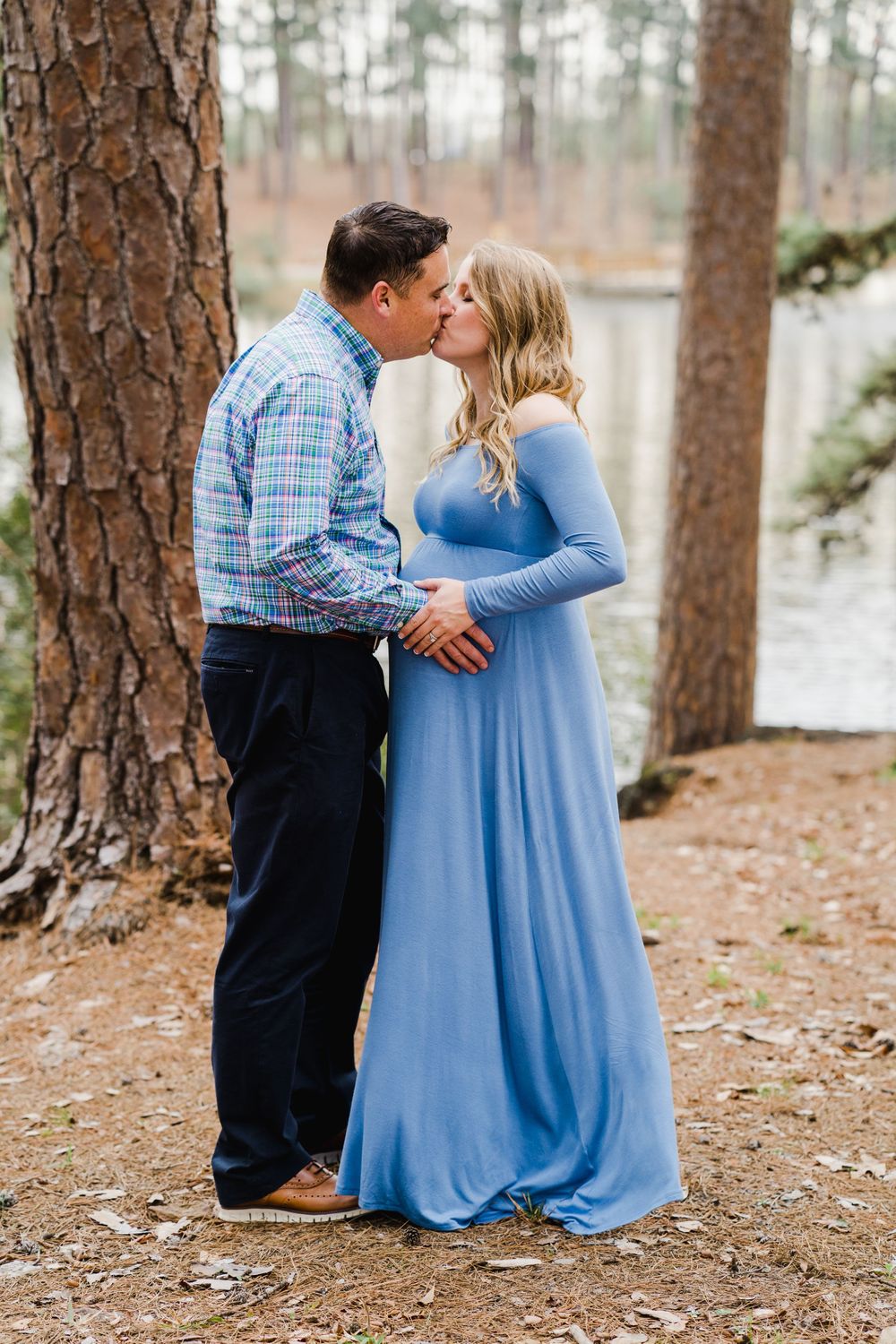 Romantic couple kisses during maternity photoshoot in natural forest setting.