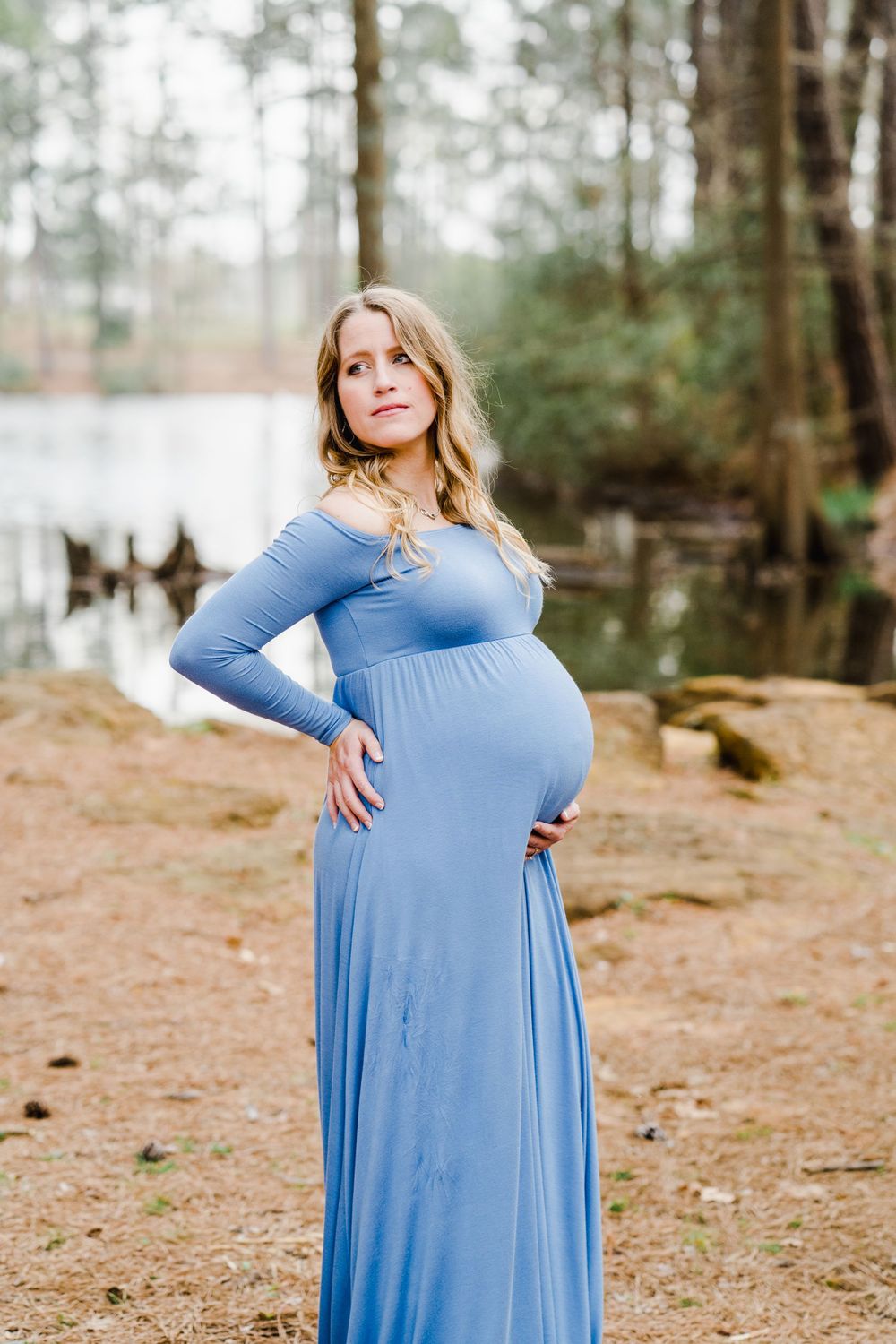 Pregnant woman in blue maxi dress poses confidently during forest maternity photoshoot.