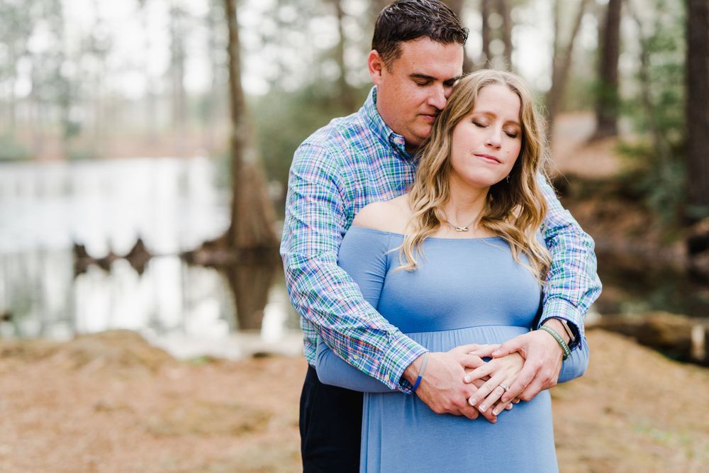 A tender maternity moment captured between a couple in blue attire against a natural forest backdrop.