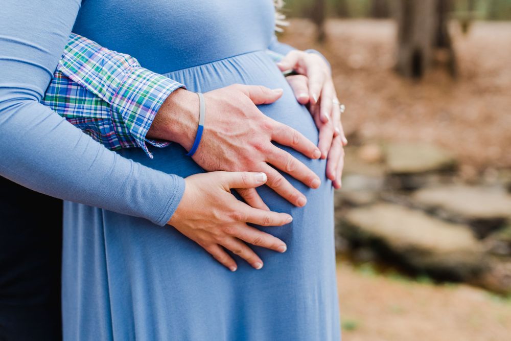 Close-up shot of hands cradling a pregnant belly in a flowing blue maternity dress.